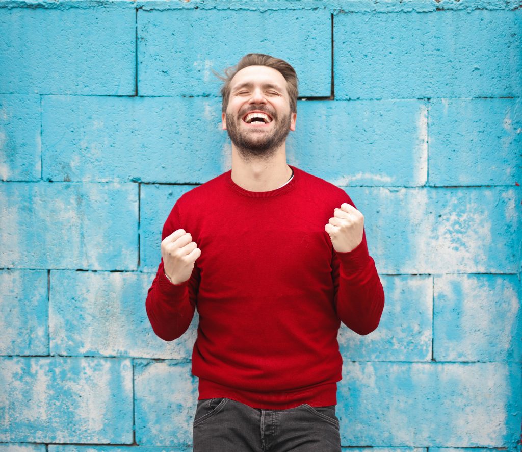 young man in red jumper with fists pumped in air, symbolising the excitement of goal setting