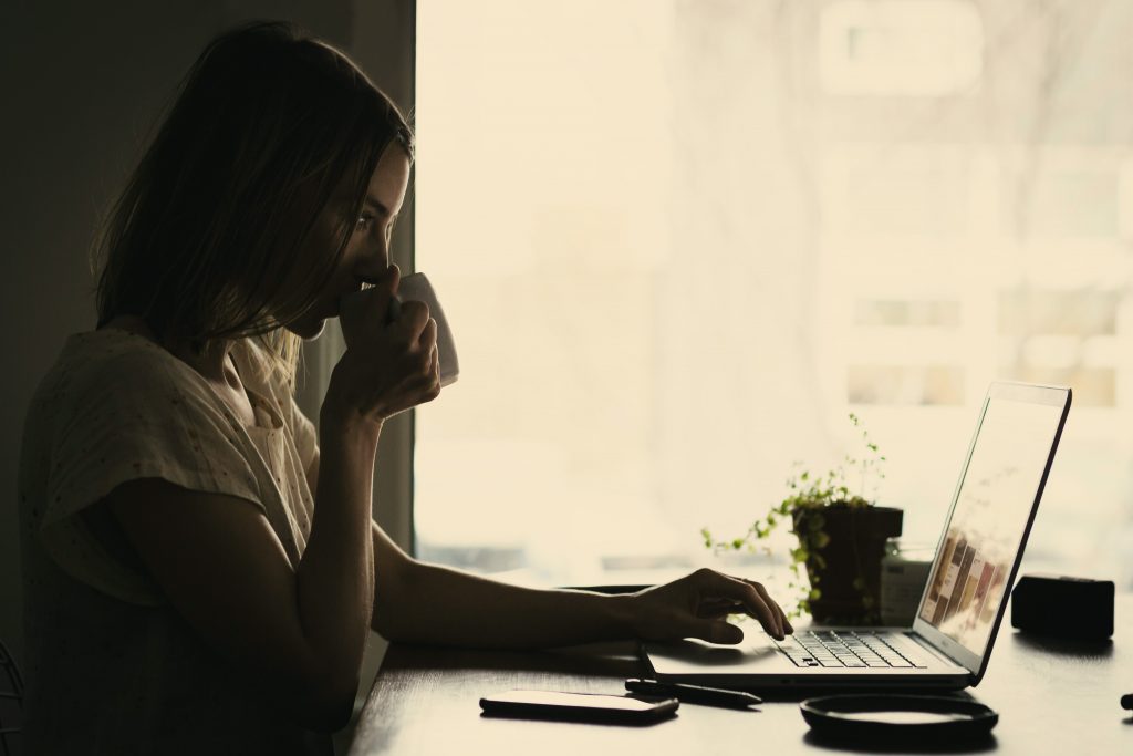 A young woman sitting at her desk drinking coffee, working on a project.