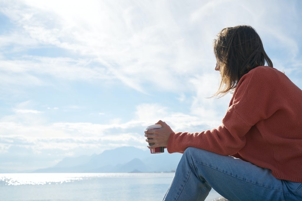 woman holding coffee looking out onto the horizon, symbolising thinking