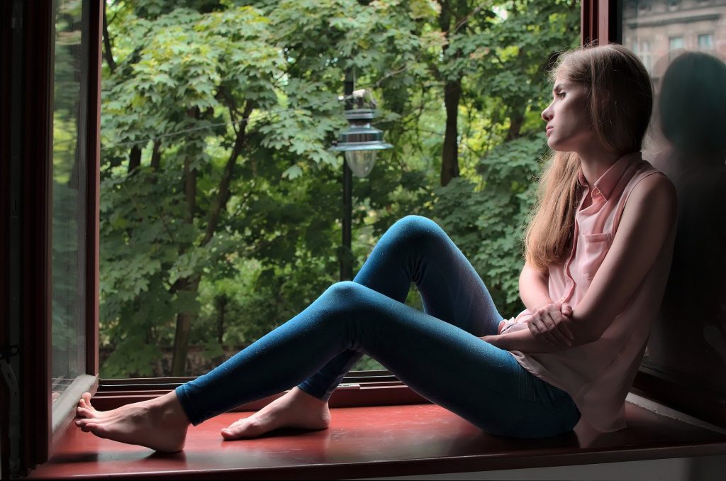woman in pink jumper looking out the window in contemplation, thinking about her future goals