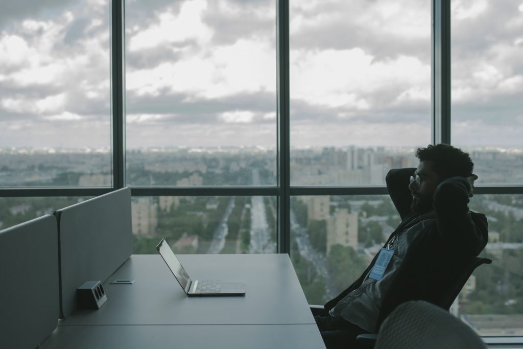 picture of a man sitting at a desk with a background of a city behind him through the window 