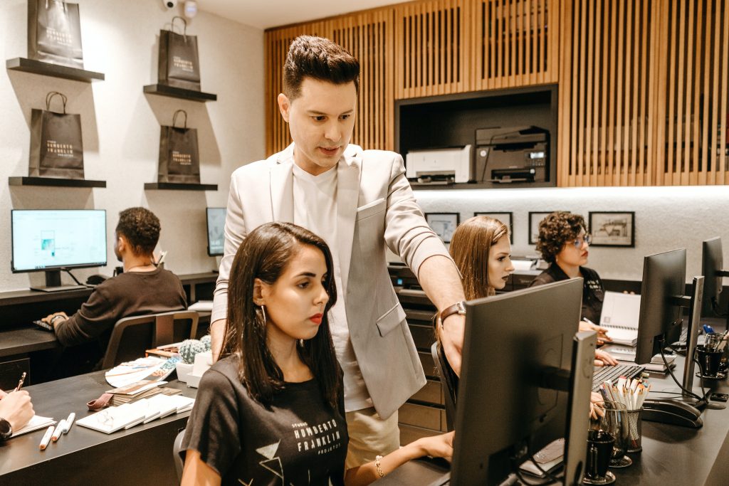 man in office standing behind woman at computer - delegating and giving instructions